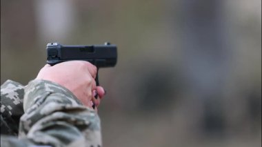 Kamuflajlı bir kadın tabancayı doğrultuyor. Kadınların güçlendirilmesi, modern savunma ve disiplinli odaklanma kavramı..