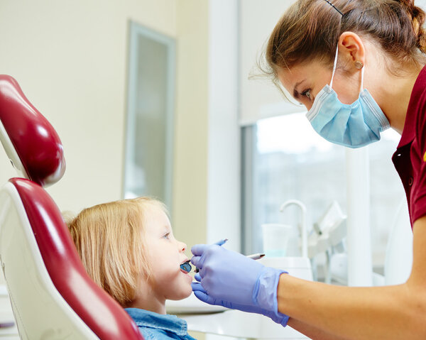 Pediatric dentist examining little girls teeth in the dentists chair
