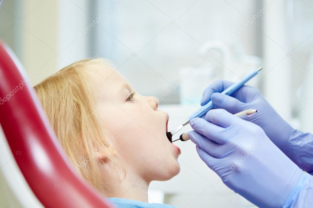 Pediatric dentist examining little girls teeth in the dentists chair