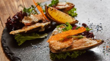 Kömürleşmiş limon ve canlı süslemelerle dokulu siyah bir levhada pişirilmiş midye çok duyusal kaplama, kaliteli gıda pazarlaması için dokunsal, mıknatıslayıcı bir görsel..