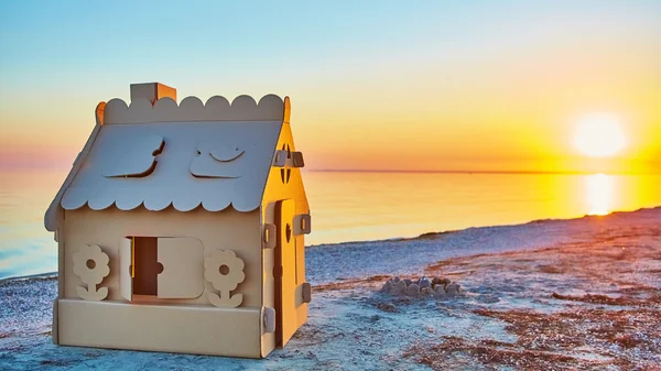 Toy house made of corrugated cardboard in the sea coast at sunset. — Stock Photo, Image