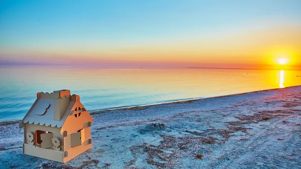 Toy house made of corrugated cardboard in the sea coast at sunset. — Stock Photo, Image