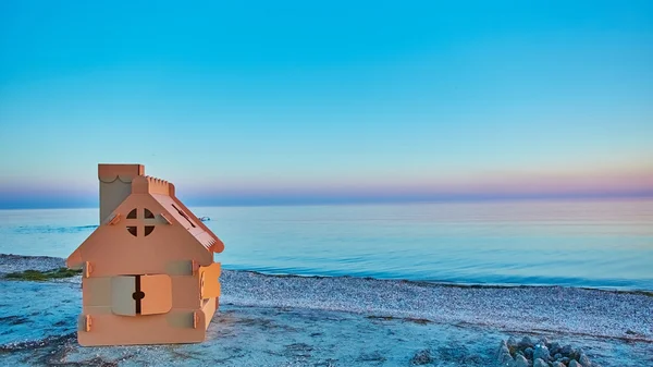 Dom zabawka wykonana z tektury falistej w brzegu morza na zachód słońca. — Zdjęcie stockowe