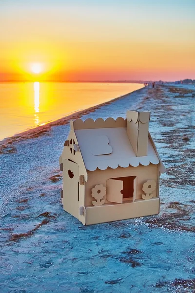 Παιχνίδι σπίτι από κυματοειδές χαρτόνι σε ακτές της θάλασσας στο ηλιοβασίλεμα. — Φωτογραφία Αρχείου