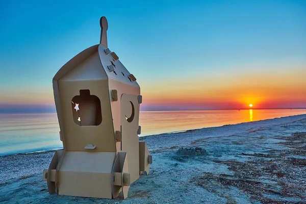 Cardboard toy spaceship at sea coast and sunset. — Stock Photo, Image