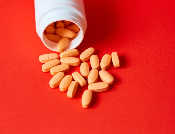 Pills spilling out of pill bottle on red. Top view with copy space. — Stock Photo, Image