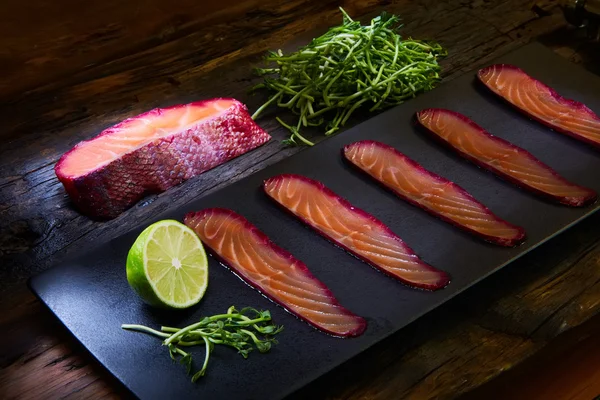 Sliced salmon fillet, sauteed with beetroot juice over black slate surface. — Stock Photo, Image