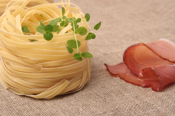 A nest of dry tagliatelle pasta on a cutting board Prosciutto Sm — Stock Photo, Image