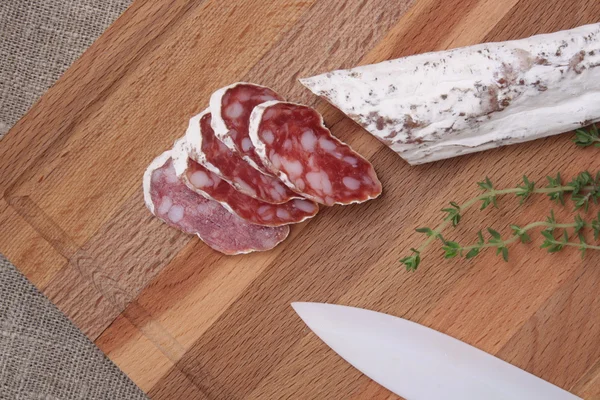 Salami slicing with thyme on board — Stock Photo, Image