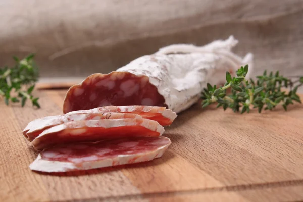 Salami slicing with thyme on board — Stock Photo, Image