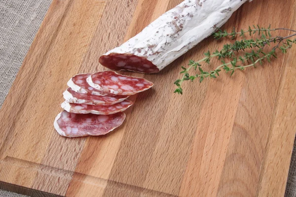 Salami slicing with thyme on board — Stock Photo, Image