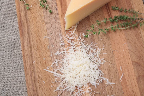 Тертый сыр пармезан и металлическая терка на деревянной пластине — стоковое фото