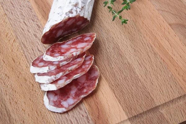 Salami slicing with thyme on board — Stock Photo, Image