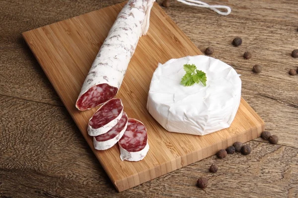 Traditional sliced salami on wooden board with brie Camembert — Stock Photo, Image