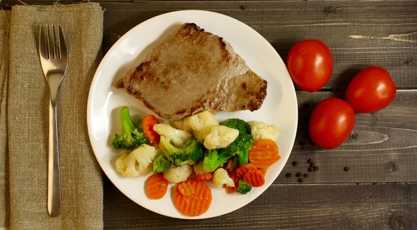 Ahşap arka planda sebzeli biftek.