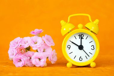 Sarı alarm saati ve turuncu arka planda çiçekler. Bahar, yaz, gün ışığı tasarruf zamanı kavramı.