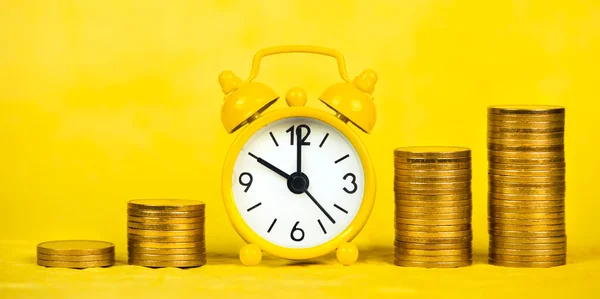 Financial freedom concept, alarm clock and gold money coins on yellow background. Web banner.