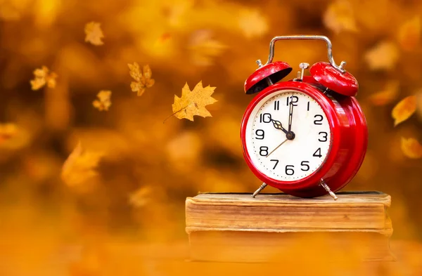 Red clock on books with leaves. Back to school in autumn, daylight savings time background.