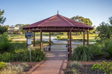Çeşme, yerli bitkiler ve güneşli Piney Gölleri Rezerv Parkı 'ndaki yeşil parkla çevrili kırmızı çatılı ahşap bir havuz, 16 Aralık 2020