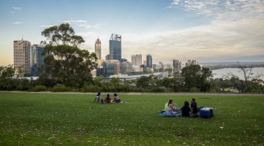 Perth City ufuk çizgisi ve nehir manzaralı çimenli tepede grup pikniği. Altın saat günbatımında, Perth, Avustralya, 25 Aralık 2020