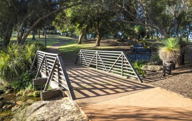 16 Aralık 2020 'de Piney Gölleri, Perth, Avustralya' da Gölgelik Ağaçları ve Su Özellikleriyle Serene Park 'ta Tahta Köprü