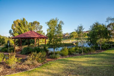 Kırmızı çatılı çardak sakin gölün yanında yerli ağaçlar ve güneşli Piney Gölleri Reserve Parkı 'nda yeşil parklar, Perth, Avustralya, 16 Aralık 2020