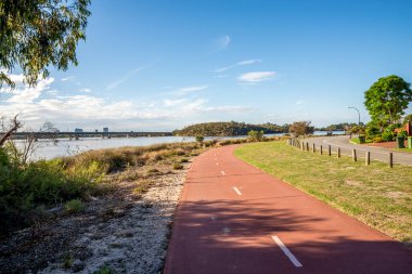 Rossmoyne banliyösündeki okaliptüs ağaçlarının altındaki Canning Nehri boyunca kırmızı kıvrımlı yol, Perth, Avustralya, 16 Mart 2021