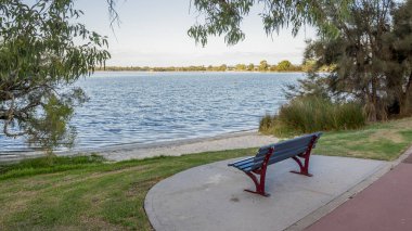 Rossmoyne banliyösünde sakin Canning Nehri 'ne bakan ağaç dalları tarafından çerçevelenmiş nehir kenarındaki bank, Perth, Avustralya, 16 Mart 2021