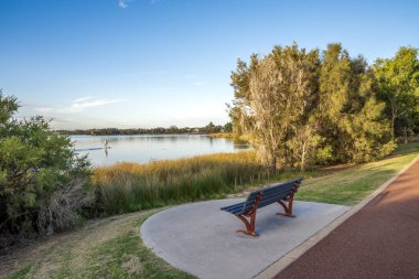 Riverside bench overlooking paddleboarder on Canning River at golden hour in Shelley suburb, Perth, Australia, 16 March 2021