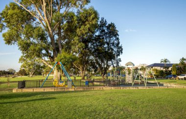 Serene lakeside park featuring towering eucalyptus trees, children's playground, and curved walking path at golden hour sunset in Shelley suburb, Perth, Australia, 16 March 2021