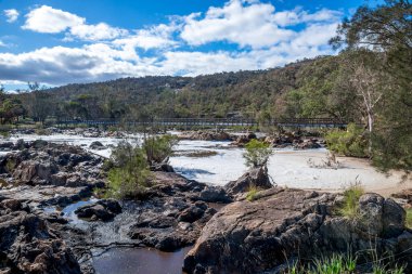 Bells Rapids Park, Kuğu Vadisi, Avustralya 'da 2 Haziran 2021' de kayalık kayalarla köpüklü akıntılar üzerinde tahta köprü.
