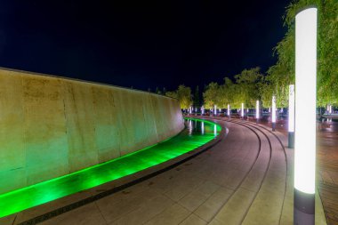 Renkli ışık aydınlatması ve ağaçlarla dolu çeşme etrafında yürüyüş yolu. Modern park tasarımı.