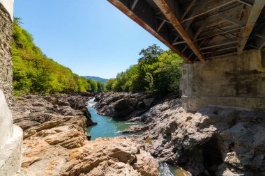 Dağlardaki bir nehrin üzerindeki metal köprü köprünün altından görünüyor..