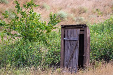 Eski ahşap tuvalet Ağaçların ve çalıların arasında bir köyde kamp kuruyor.