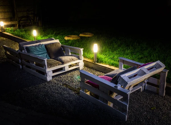 Night garden with self-made couch from pallets is illuminated garden lamps