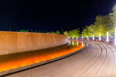 Renkli ışık aydınlatması ve ağaçlarla dolu çeşme etrafında yürüyüş yolu. Modern park tasarımı.