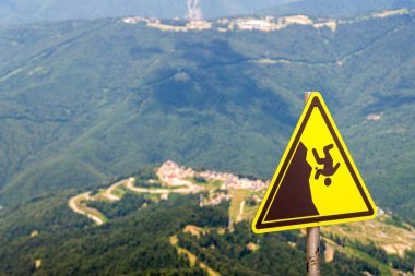 Düşen adamın sembolü olan sarı uyarı işareti. Arka planda büyük bir yaz dağı, kayalar.