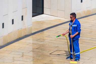 Rusya, Krasnodar, 29 Nisan 2019: Sokak işçisi su kaynaklarına bağlı bir hortumla kaldırımı yıkıyor..