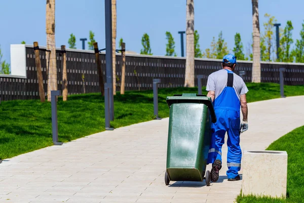 清掃員がゴミ缶を車輪に転がす 近代的な公園での清掃サービス — ストック写真