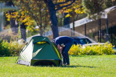Genç bir adam şehir parkında kurulmuş bir çadıra bakıyor..