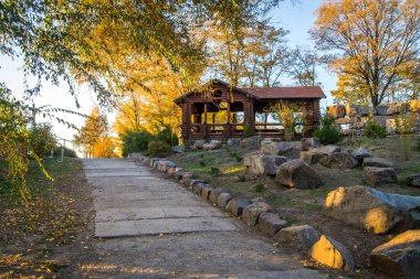Nehir kenarındaki ahşap evler ve banklarla sonbahar manzarası,