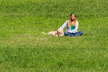 Portekiz, Lizbon, 09 Ekim 2018: Güneşli bir günde yeşil çimlerin üzerinde köpeği olan genç ve güzel Portekizli kadın.