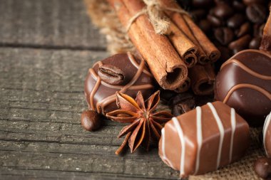 Koyu, beyaz ve sütlü çikolata yığını, cips çeşitleri. Kaba ahşap arka planda çikolata ve kahve çekirdekleri. Baharatlar, tarçın. Seçici makro odaklanma. Çikolata arkaplanı. Tatlılar