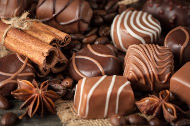 Koyu, beyaz ve sütlü çikolata yığını, cips çeşitleri. Kaba ahşap arka planda çikolata ve kahve çekirdekleri. Baharatlar, tarçın. Seçici makro odaklanma. Çikolata arkaplanı. Tatlılar