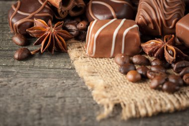 Koyu, beyaz ve sütlü çikolata yığını, cips çeşitleri. Kaba ahşap arka planda çikolata ve kahve çekirdekleri. Baharatlar, tarçın. Seçici makro odaklanma. Çikolata arkaplanı. Tatlılar