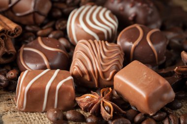 Koyu, beyaz ve sütlü çikolata yığını, cips çeşitleri. Kaba ahşap arka planda çikolata ve kahve çekirdekleri. Baharatlar, tarçın. Seçici makro odaklanma. Çikolata arkaplanı. Tatlılar