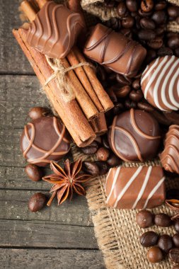 Koyu, beyaz ve sütlü çikolata yığını, cips çeşitleri. Kaba ahşap arka planda çikolata ve kahve çekirdekleri. Baharatlar, tarçın. Seçici makro odaklanma. Çikolata arkaplanı. Tatlılar