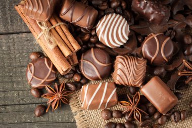 Koyu, beyaz ve sütlü çikolata yığını, cips çeşitleri. Kaba ahşap arka planda çikolata ve kahve çekirdekleri. Baharatlar, tarçın. Seçici makro odaklanma. Çikolata arkaplanı. Tatlılar