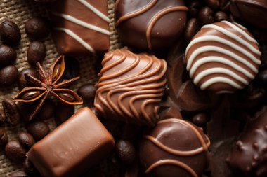 Koyu, beyaz ve sütlü çikolata yığını, cips çeşitleri. Kaba ahşap arka planda çikolata ve kahve çekirdekleri. Baharatlar, tarçın. Seçici makro odaklanma. Çikolata arkaplanı. Tatlılar