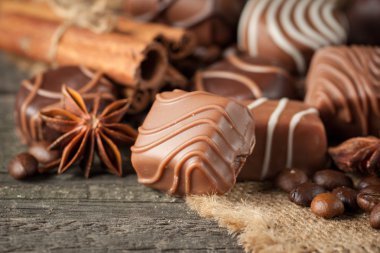 Koyu, beyaz ve sütlü çikolata yığını, cips çeşitleri. Kaba ahşap arka planda çikolata ve kahve çekirdekleri. Baharatlar, tarçın. Seçici makro odaklanma. Çikolata arkaplanı. Tatlılar